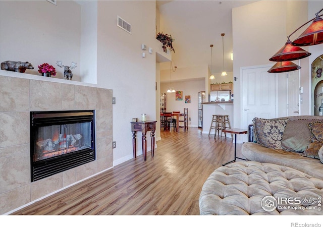 living room featuring light wood-type flooring, a high ceiling, and a tiled fireplace