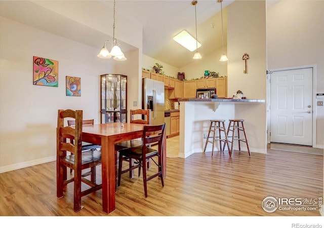 dining area featuring light wood-style floors, a chandelier, high vaulted ceiling, and baseboards