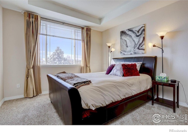 carpeted bedroom with a tray ceiling and baseboards