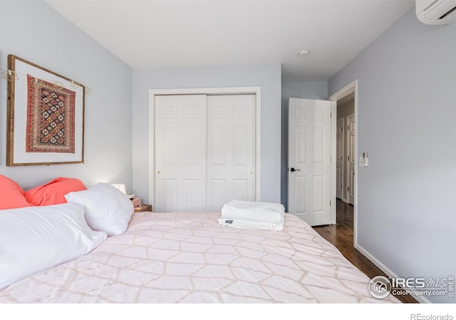 bedroom with a closet, baseboards, dark wood-style flooring, and a wall mounted AC