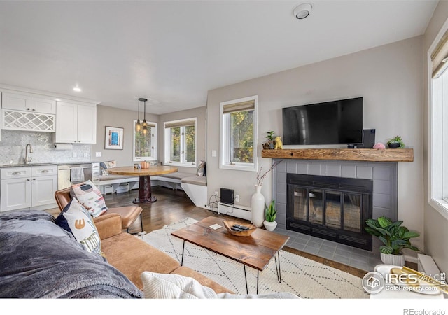 living area with a baseboard heating unit, a tiled fireplace, recessed lighting, wet bar, and wood finished floors