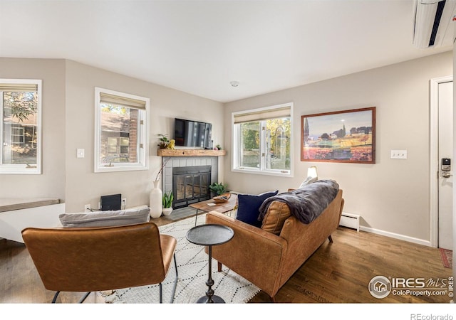 living room with a baseboard heating unit, baseboards, wood finished floors, and a tile fireplace