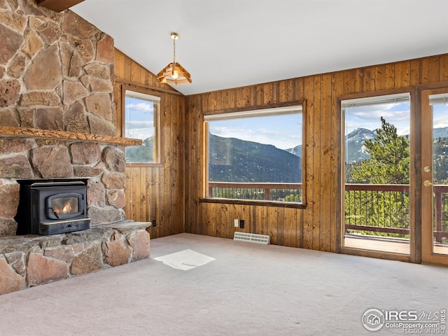 carpeted living room featuring a mountain view, vaulted ceiling, a wood stove, and a healthy amount of sunlight