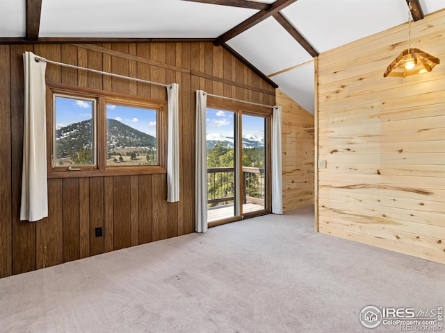 empty room featuring wood walls, a mountain view, carpet floors, and vaulted ceiling with beams