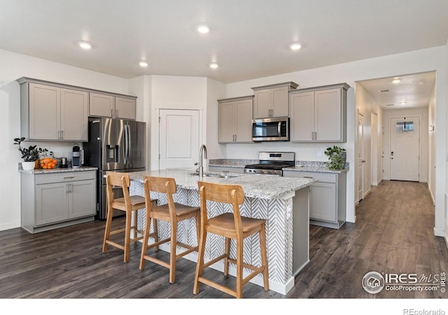 kitchen with a kitchen bar, gray cabinets, stainless steel appliances, and a kitchen island with sink