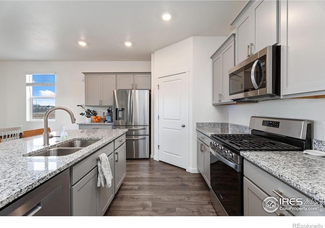 kitchen with appliances with stainless steel finishes, gray cabinetry, sink, light stone counters, and dark hardwood / wood-style floors