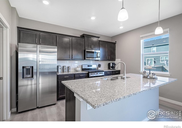 kitchen with sink, hanging light fixtures, appliances with stainless steel finishes, and an island with sink