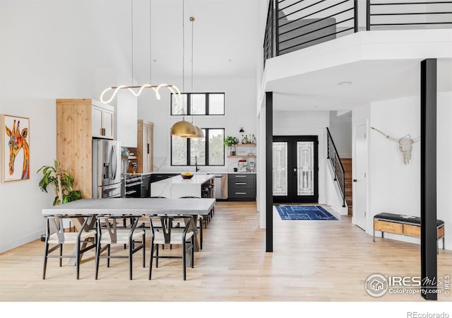 dining area featuring sink, a towering ceiling, light hardwood / wood-style flooring, and french doors