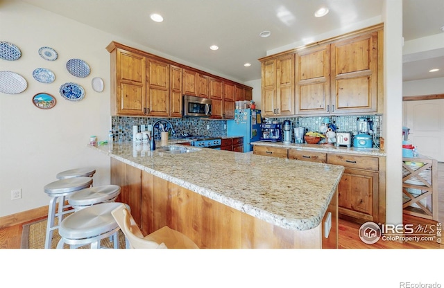 kitchen with light stone countertops, a kitchen breakfast bar, sink, refrigerator, and kitchen peninsula