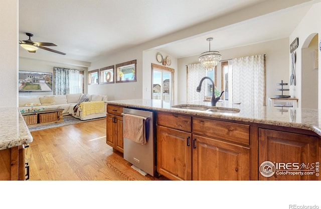 kitchen with light stone countertops, a wealth of natural light, dishwasher, sink, and light wood-type flooring