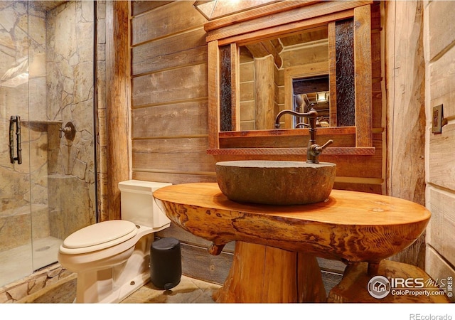 bathroom with a shower with shower door, sink, toilet, and wood walls