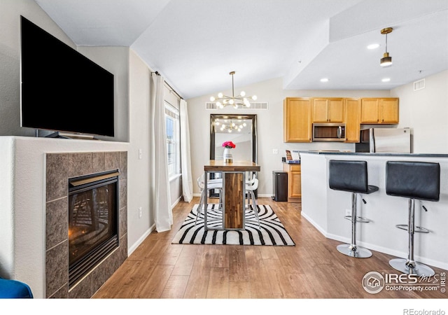 kitchen with vaulted ceiling, light hardwood / wood-style flooring, light brown cabinets, pendant lighting, and stainless steel appliances