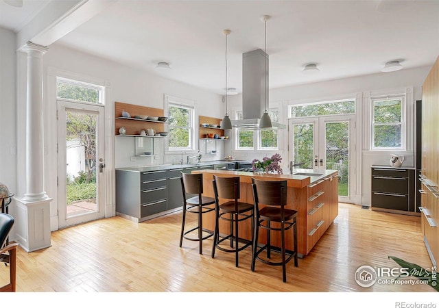 kitchen with decorative columns, a center island with sink, sink, and island range hood