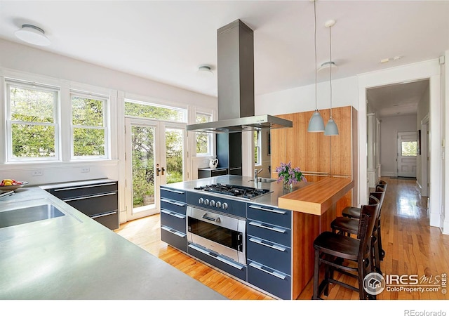 kitchen featuring pendant lighting, a kitchen bar, light hardwood / wood-style floors, island range hood, and stainless steel gas cooktop