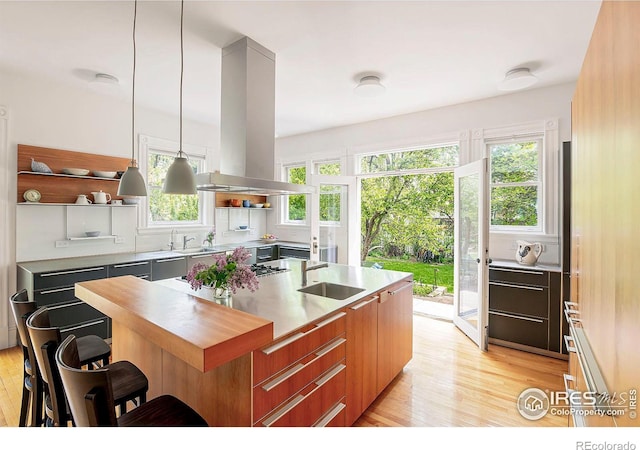 kitchen featuring decorative light fixtures, island exhaust hood, an island with sink, sink, and a breakfast bar area