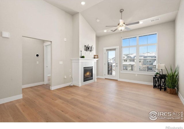 unfurnished living room with ceiling fan, a tile fireplace, and light hardwood / wood-style flooring