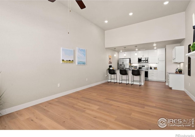 kitchen with a towering ceiling, white cabinetry, a kitchen breakfast bar, light hardwood / wood-style floors, and stainless steel appliances