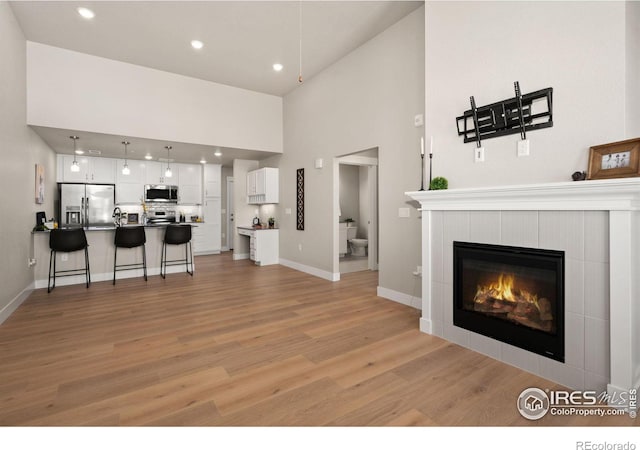 living room with a towering ceiling, a tile fireplace, and light hardwood / wood-style flooring