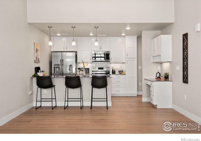 kitchen featuring decorative light fixtures, stainless steel appliances, white cabinets, and a kitchen bar