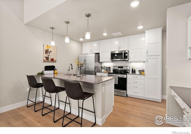 kitchen with decorative light fixtures, white cabinetry, a kitchen breakfast bar, decorative backsplash, and stainless steel appliances