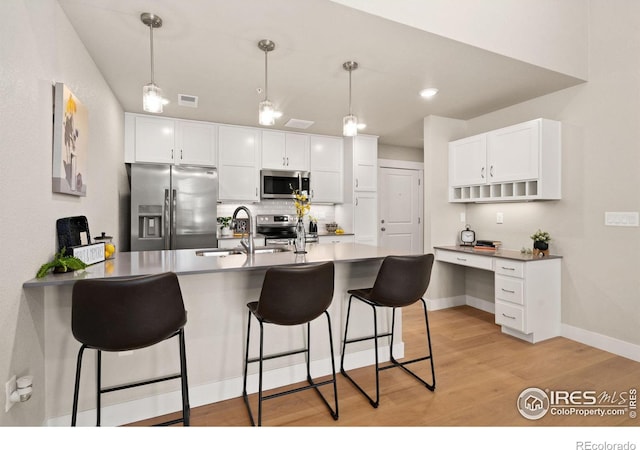 kitchen with sink, light wood-type flooring, pendant lighting, stainless steel appliances, and white cabinets