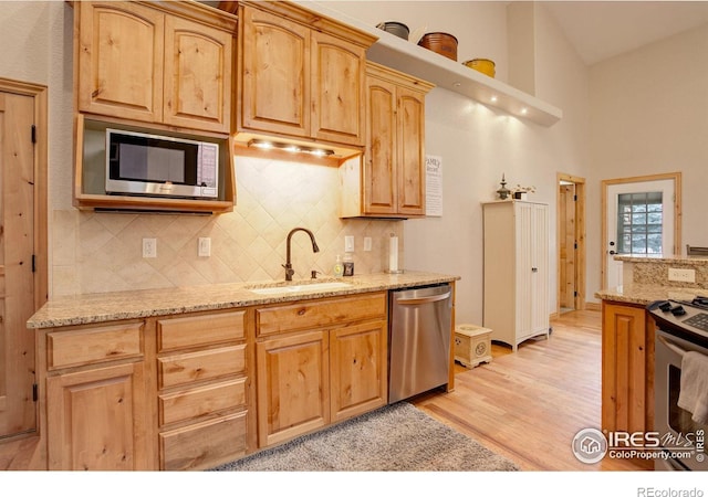 kitchen with decorative backsplash, sink, light hardwood / wood-style flooring, stainless steel appliances, and light stone counters