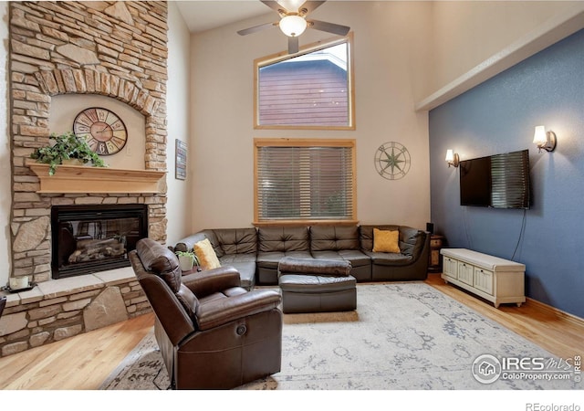 living room with ceiling fan, a stone fireplace, hardwood / wood-style floors, and high vaulted ceiling