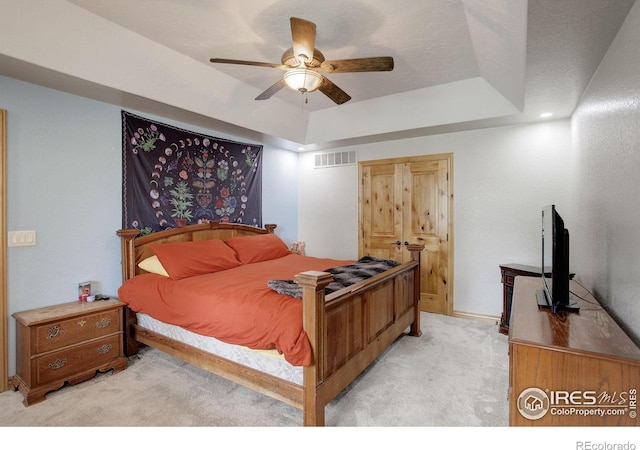 bedroom with ceiling fan, a raised ceiling, and light carpet