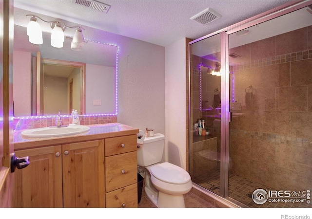 bathroom with a textured ceiling, toilet, a shower with door, and vanity