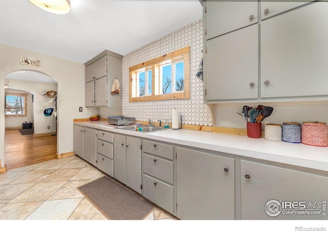 kitchen featuring decorative backsplash, sink, light tile patterned floors, and gray cabinetry