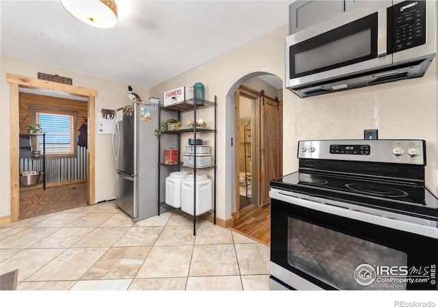 kitchen with light tile patterned flooring, a barn door, and appliances with stainless steel finishes