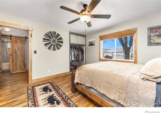 bedroom featuring light hardwood / wood-style flooring, a closet, ceiling fan, and a barn door