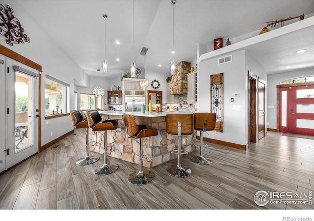 kitchen featuring kitchen peninsula, hanging light fixtures, stainless steel built in refrigerator, high vaulted ceiling, and a breakfast bar area