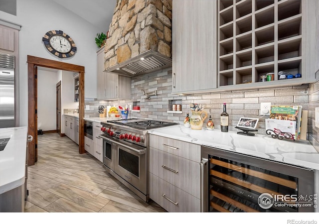 kitchen with beverage cooler, high end appliances, premium range hood, backsplash, and light stone counters