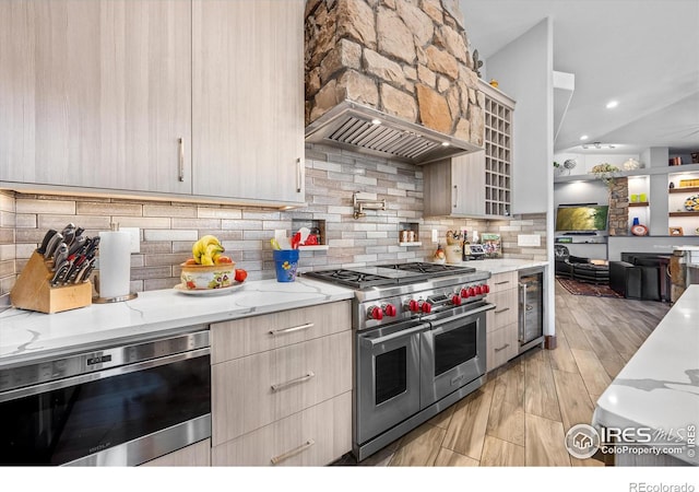 kitchen with light hardwood / wood-style floors, tasteful backsplash, premium range hood, light stone counters, and range with two ovens