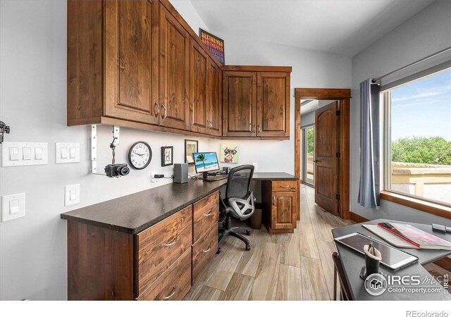 office area featuring light hardwood / wood-style floors, lofted ceiling, and built in desk