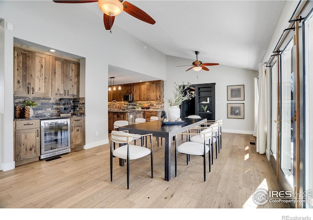 dining space with light hardwood / wood-style flooring, vaulted ceiling, beverage cooler, and a wealth of natural light