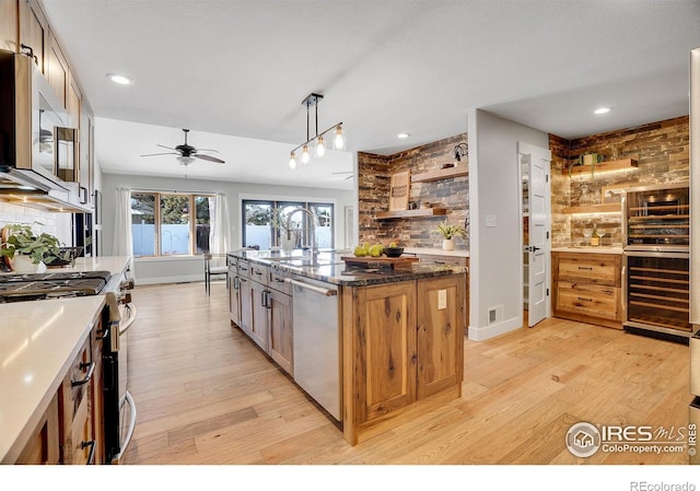 kitchen with pendant lighting, stainless steel appliances, dark stone countertops, a kitchen island with sink, and light wood-type flooring