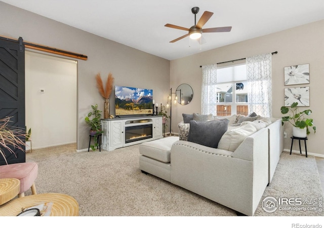 living room with carpet floors, a barn door, a glass covered fireplace, ceiling fan, and baseboards