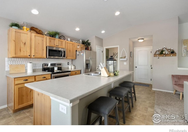 kitchen with a kitchen breakfast bar, a sink, vaulted ceiling, stainless steel appliances, and backsplash