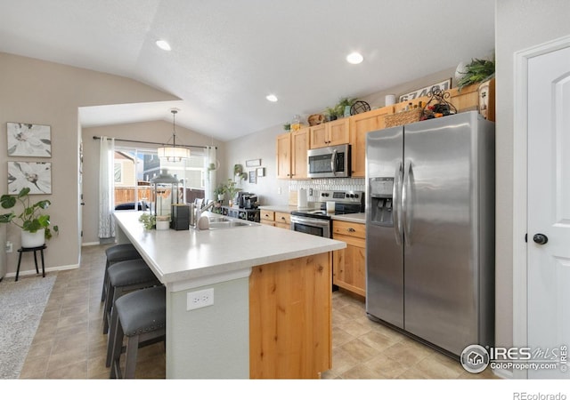 kitchen featuring a breakfast bar area, a sink, vaulted ceiling, appliances with stainless steel finishes, and decorative light fixtures