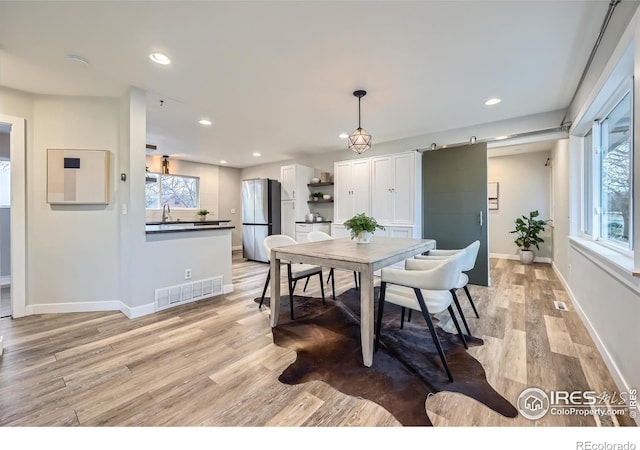 dining space featuring light wood-type flooring, a wealth of natural light, and a barn door