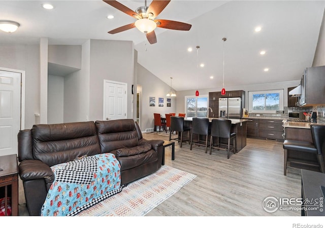 living room featuring sink, light hardwood / wood-style flooring, high vaulted ceiling, and ceiling fan