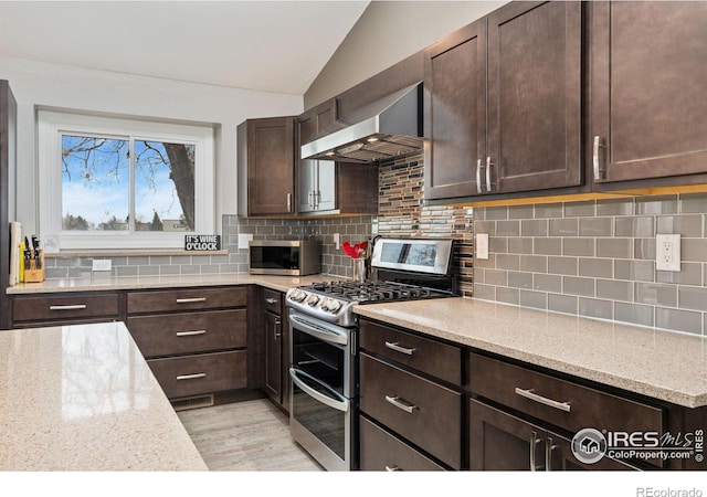 kitchen with light stone countertops, appliances with stainless steel finishes, backsplash, wall chimney exhaust hood, and lofted ceiling