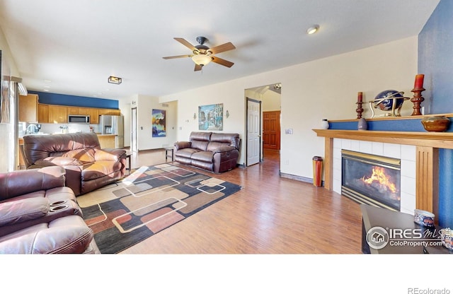 living room featuring ceiling fan, a tile fireplace, and light hardwood / wood-style flooring