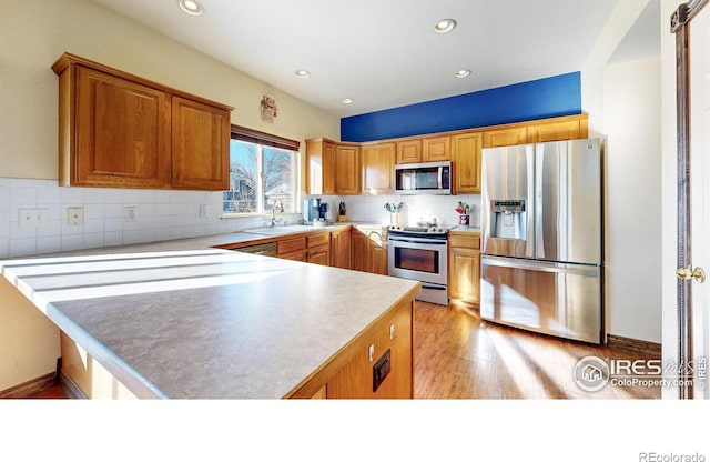 kitchen featuring kitchen peninsula, appliances with stainless steel finishes, sink, backsplash, and light hardwood / wood-style floors