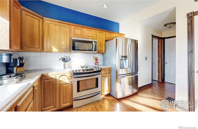 kitchen with backsplash, appliances with stainless steel finishes, and light hardwood / wood-style flooring