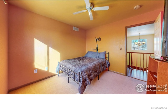 carpeted bedroom with ceiling fan with notable chandelier