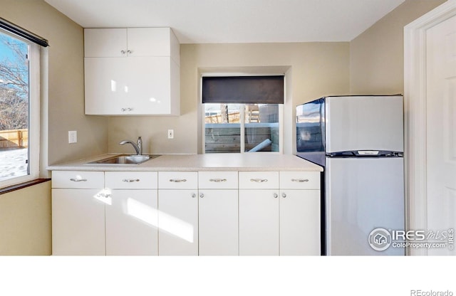 kitchen featuring sink, white cabinetry, and stainless steel refrigerator