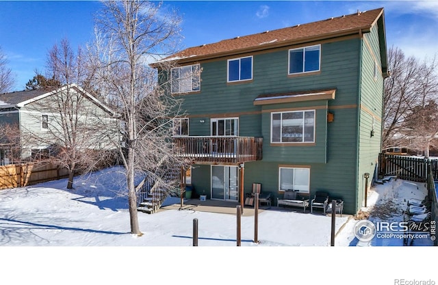 snow covered back of property with a wooden deck